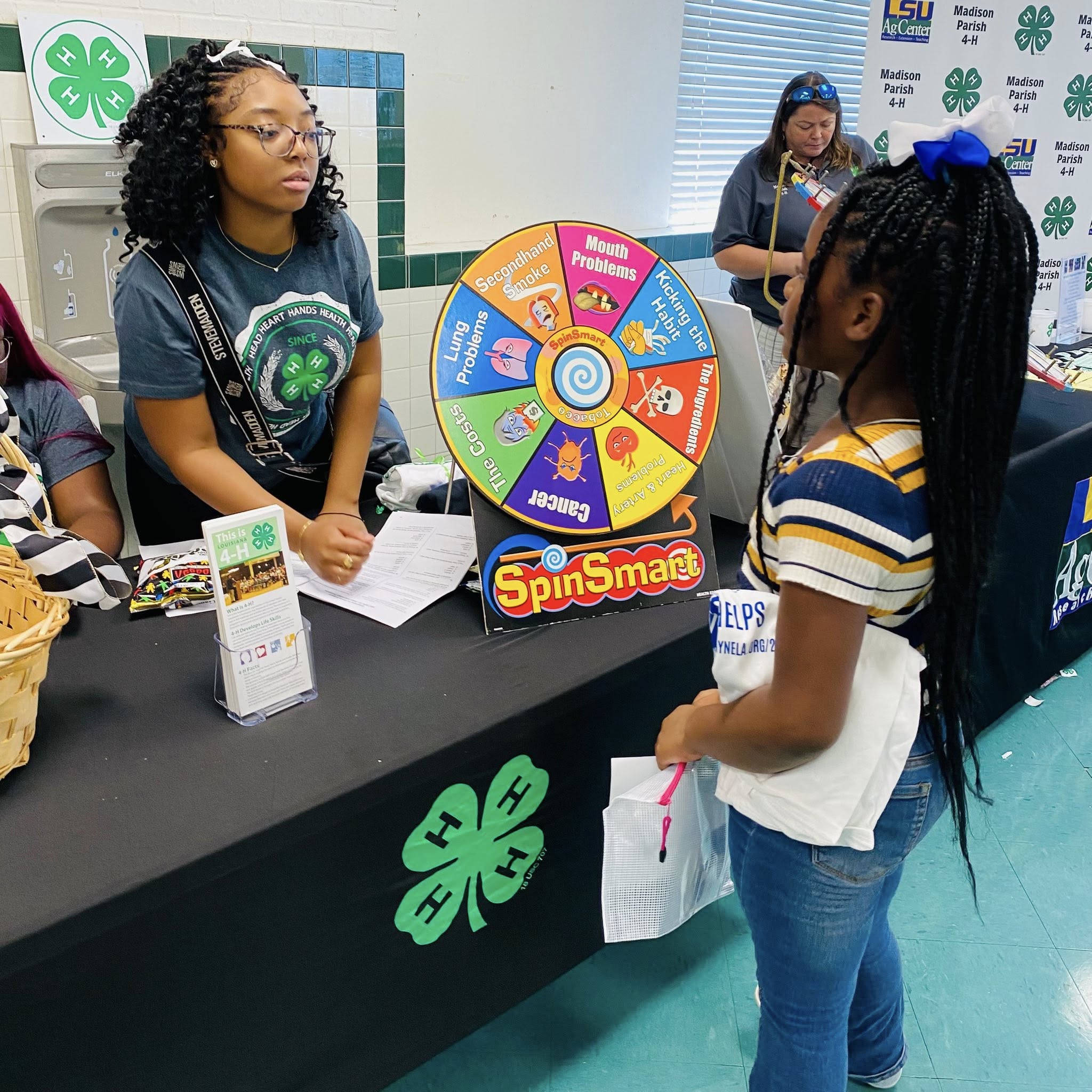 A teenage girl at a table talking to a younger girl.